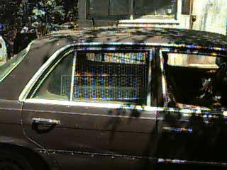 photo of exterior of car with open window blocked by a barrier made from a refridgerator shelf.