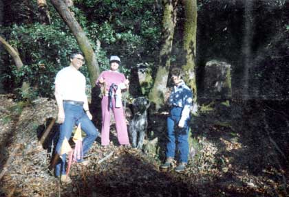 Victory photo from Bones' TDX,  showing a wooded section of the track. Dog and  handler displaying articles, flanked by the two judges.